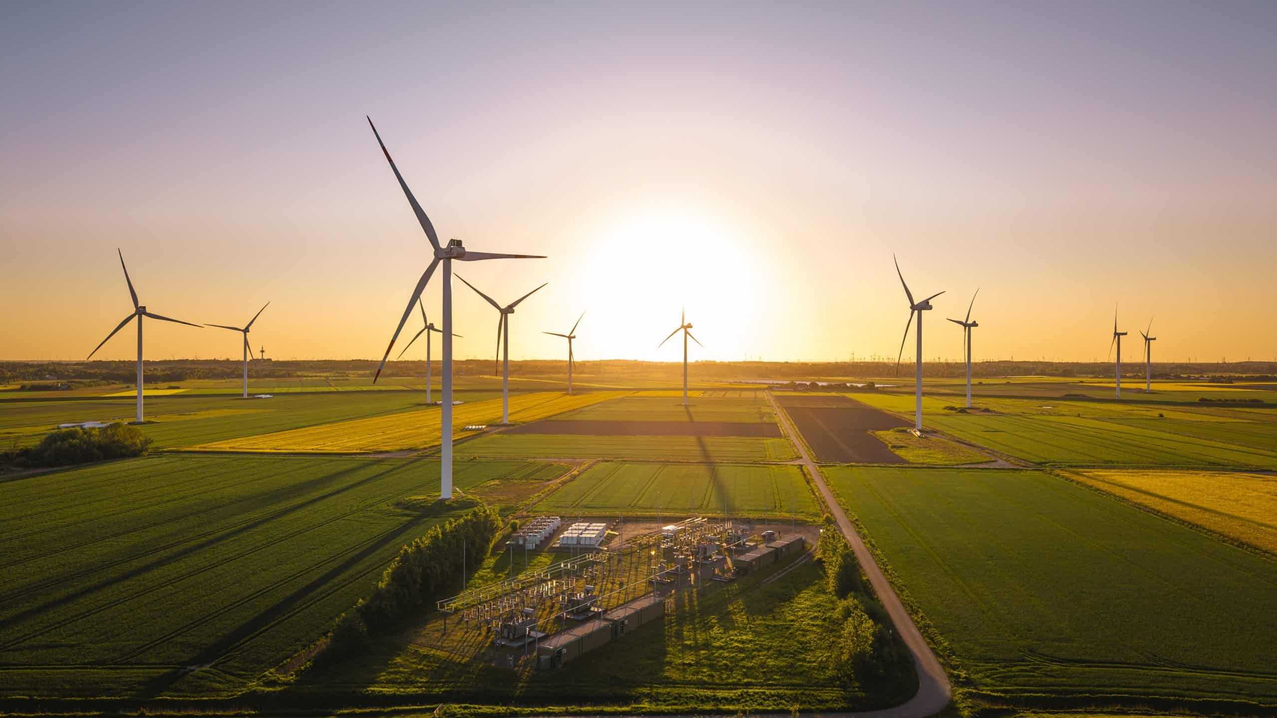 Windkraftanlagen auf landwirtschaftlichen Feldern bei Sonnenuntergang für erneuerbare Energien.